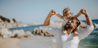 father holding young daughter on his shoulders at the beach