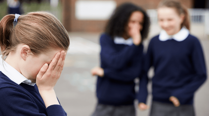 young girl in foreground with hands covering face and two girls laughing in the background